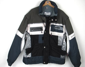May include: A black, grey and white ski jacket with the word "dublin" on the front and the word "racing" on the left sleeve.