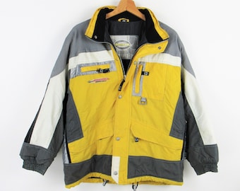 Pode incluir: Casaco de inverno multicolorido com um design amarelo, cinza, branco e preto. O casaco tem gola alta, vários bolsos e fecho de zíper. O casaco está pendurado em um cabide de madeira.