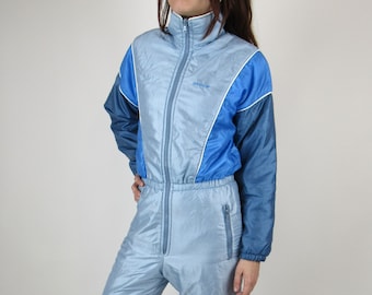 May include: A light blue ski jumpsuit with white and blue accents. The jumpsuit has a zipper closure and a logo that says "adidas" on the chest.