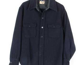 May include: A navy blue wool shirt with a button-down collar and two flap pockets. The shirt has a long sleeve and is made of a thick, warm fabric.