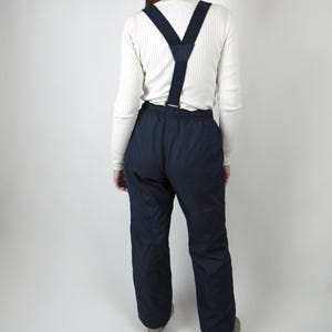 May include: A pair of dark blue ski pants with suspenders. The pants have a zipper fly and two front pockets.
