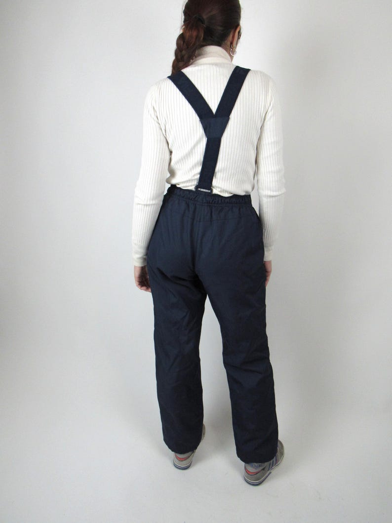May include: A pair of dark blue ski pants with suspenders. The pants have a zipper fly and two front pockets.