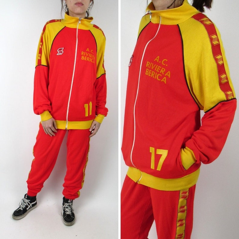 Puede incluir: Ch&aacute;ndal rojo y amarillo con una chaqueta con cremallera. La chaqueta tiene el texto "A.C. RIVIERA BERICA" y el n&uacute;mero "17". El pantal&oacute;n tiene rayas amarillas a los lados.