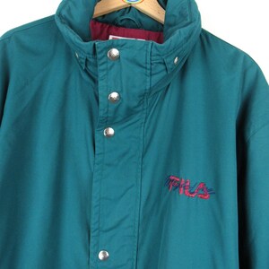 May include: Teal blue vintage Fila jacket with a red embroidered logo. The jacket has a high collar and a snap closure.