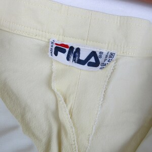 May include: A close-up of a yellow garment with a white Fila label that reads "Made in Italy" and has size information in centimeters.