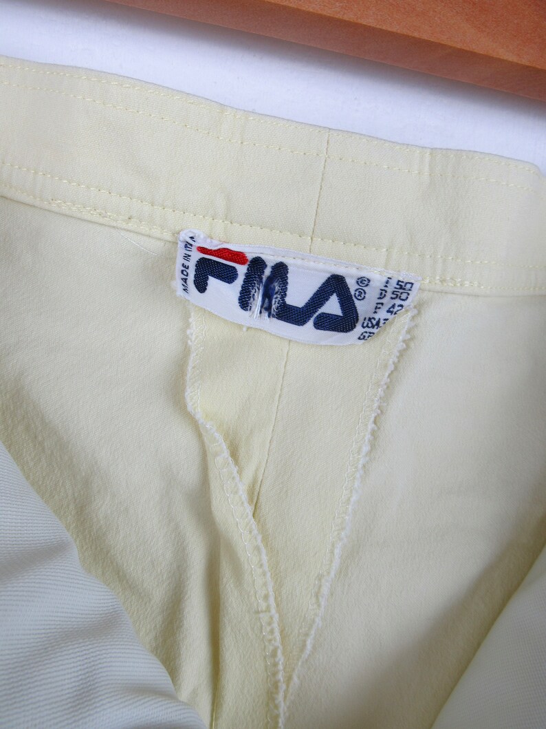 May include: A close-up of a yellow garment with a white Fila label that reads "Made in Italy" and has size information in centimeters.