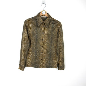 Pode incluir: Uma camisa de botões de manga comprida com estampa de pele de cobra em tons de marrom e dourado.