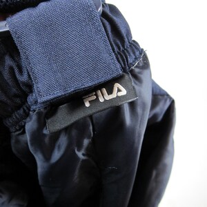 May include: Close-up of a navy blue drawstring waistband with a black label that reads "FILA" in white lettering.