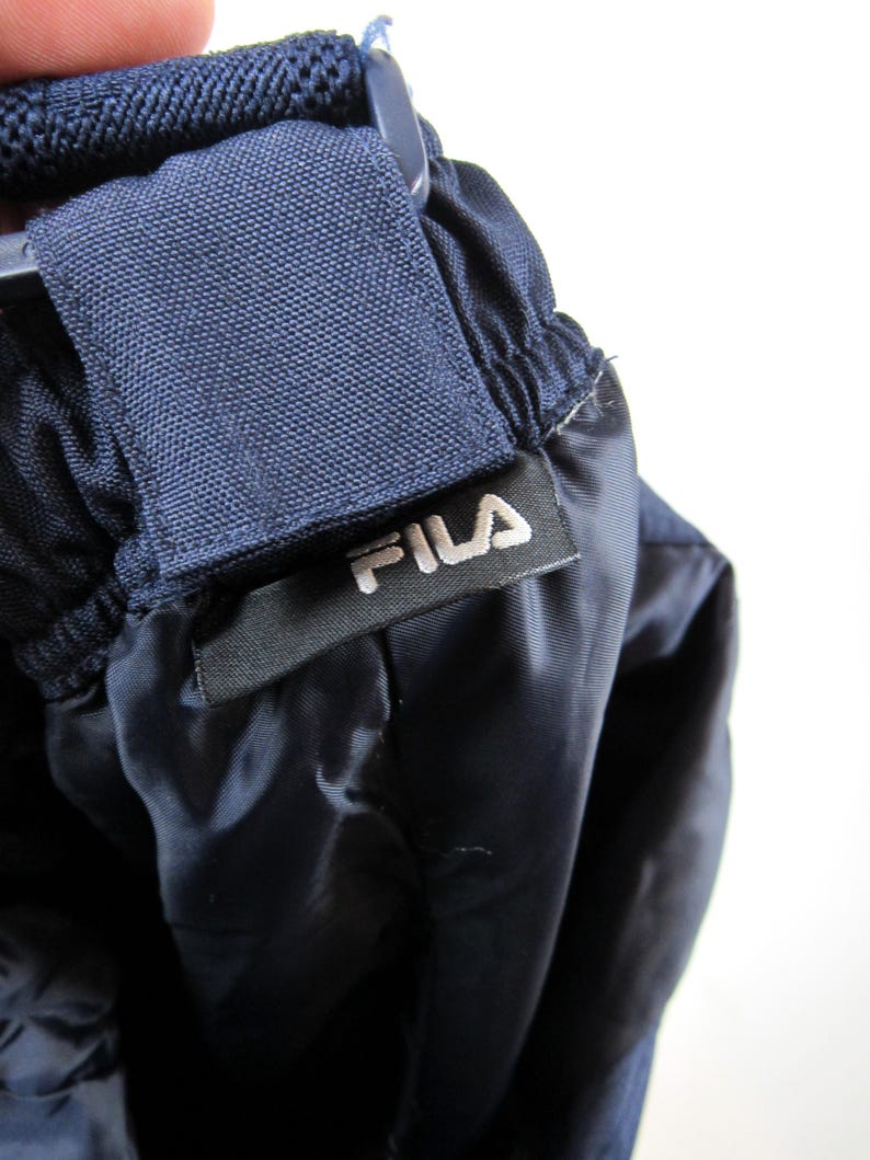 May include: Close-up of a navy blue drawstring waistband with a black label that reads "FILA" in white lettering.