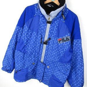 May include: A blue FILA winter jacket with a geometric pattern. The jacket features a high collar, a full-length zipper, and the FILA logo on the chest. The jacket has a black and gray color scheme.