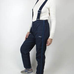 May include: Navy blue ski pants with a blue stripe down the side and a FILA logo. The pants have suspenders and are made of a water-resistant material.
