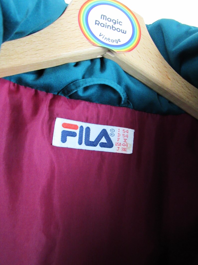 May include: A teal blue Fila jacket with a maroon lining. The jacket has a size tag that reads "I 54 D 54 F Y USA 44 J 34L".
