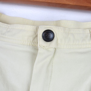 May include: Close-up of a light yellow pair of pants with a black button featuring a stylized letter "F".