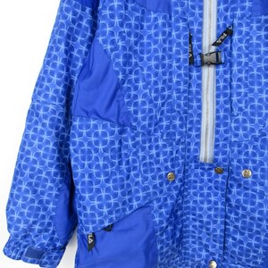 May include: A blue and white patterned jacket with a zipper closure and snap buttons. The jacket has a geometric design and the brand name "FILA" is visible on the zipper and pocket.