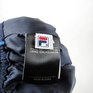 May include: A navy blue and white Fila brand label with the text "SHELL: 100% POLYESTER LINING: 100% POLYESTER MADE IN CHINA".