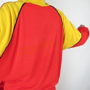 Puede incluir: Sudadera roja y amarilla con ribetes negros y la palabra "COFFIN" impresa en la espalda.