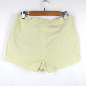 May include: A pair of pale yellow shorts hanging on a wooden hanger. The shorts have a simple design and a straight leg.