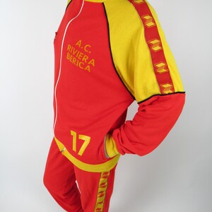 Puede incluir: Ch&aacute;ndal rojo y amarillo con el texto "A.C. RIVIERA BERICA" y el n&uacute;mero "17" en la parte delantera.