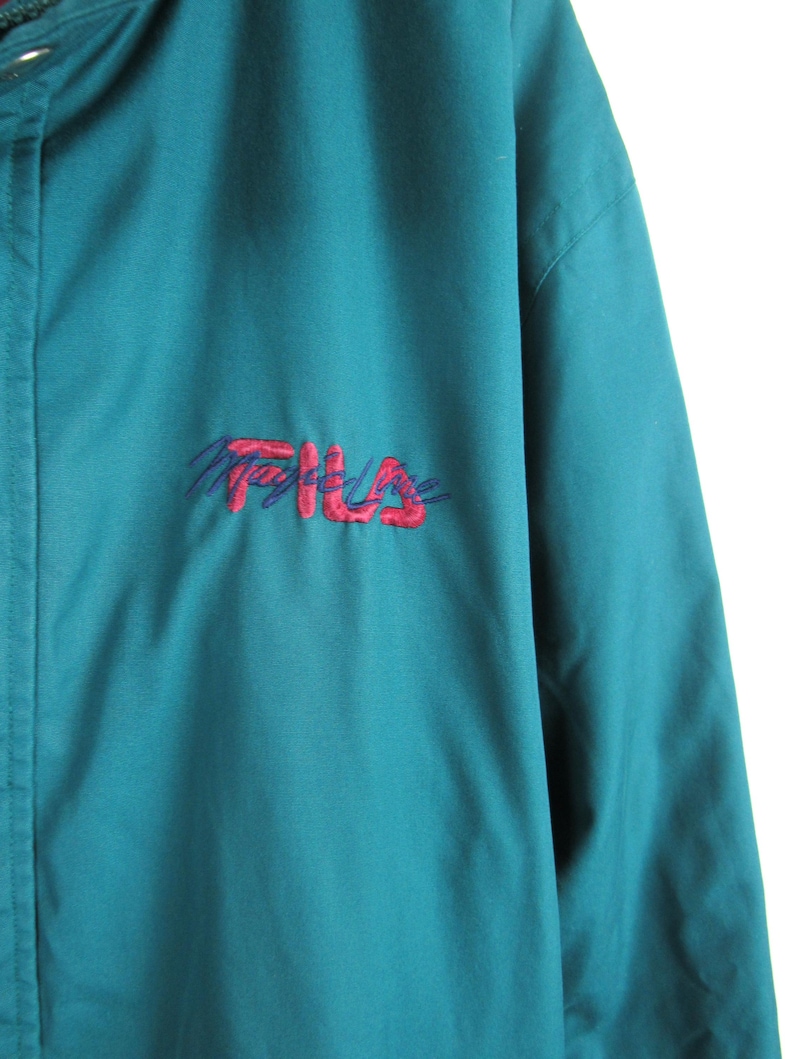 May include: Teal blue jacket with a red and purple embroidered Fila logo.