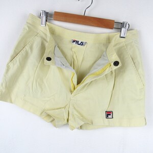 May include: A pair of yellow athletic shorts with a red and blue Fila logo on the right leg and a Fila logo on the waistband.