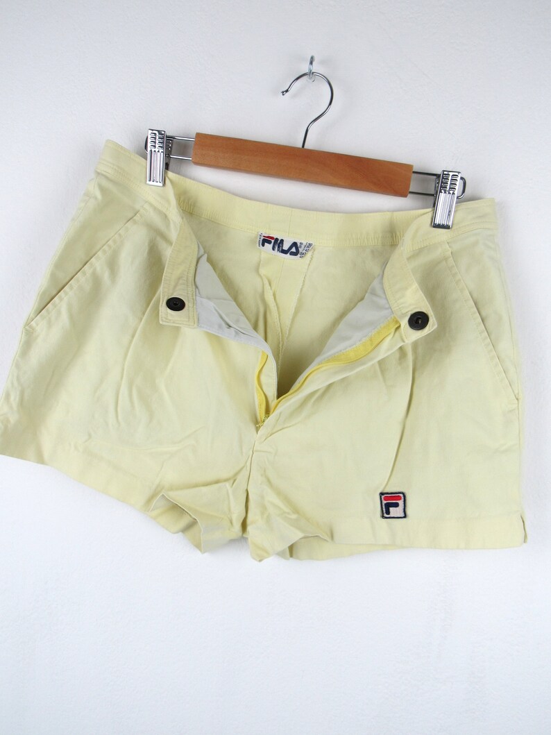 May include: A pair of yellow athletic shorts with a red and blue Fila logo on the right leg and a Fila logo on the waistband.