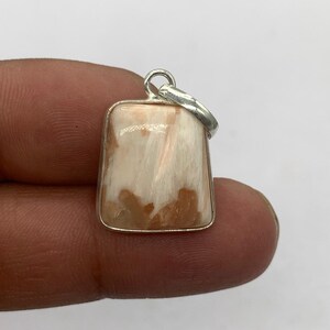 May include: A rectangular pendant with a silver bail. The pendant features a cream-colored stone with brown and white marbling. The stone is set in a silver bezel.