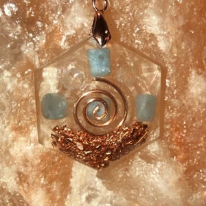 May include: A clear hexagonal pendant with a copper wire spiral and blue aquamarine crystals. The pendant is set in a clear resin and has a gold-colored bail.