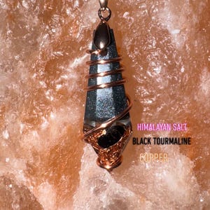 Könnte beinhalten: Eine Anhängerkette mit einem dunklen, facettierten Stein, der in Kupferdraht gewickelt ist. Der Anhänger hängt an einer schwarzen Kordel. Der Text auf dem Bild lautet: "Himalayan Salt, Black Tourmaline, Copper."