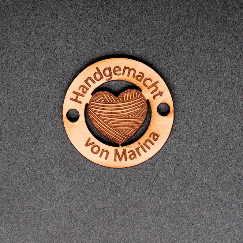 May include: A round wooden tag with the text "Handgemacht von Marina" and a heart-shaped design in the center.