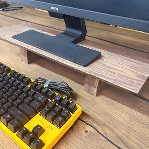 May include: A wooden monitor stand with a dark wood grain finish supporting a black BenQ computer monitor. In the foreground, a bright yellow mechanical keyboard with black keys and the brand name HATOR printed on the frame is visible.