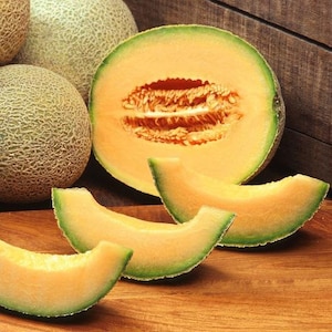 May include: A close-up of a cantaloupe melon cut in half, revealing the orange flesh and seeds. There are also four slices of cantaloupe melon on a wooden surface.