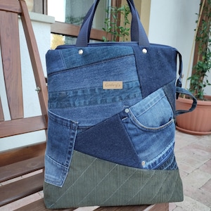 Op de afbeelding: Een draagtas gemaakt van een patchwork van verschillende blauwe spijkerstofstukken en een effen olijfgroen corduroy paneel aan de onderkant. De tas heeft twee donkerblauwe stoffen handvatten, een ritssluiting aan de bovenkant en een bruin label met Godry's.