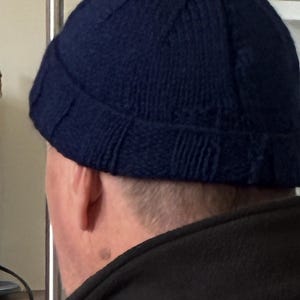 Peut inclure: Un bonnet en tricot bleu marine foncé doté d'un revers côtelé et d'une construction texturée à plusieurs panneaux. Le bonnet est confectionné avec un motif de fil uniforme, présentant un design classique à couronne arrondie bien ajusté.