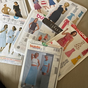 May include: A collection of seven paper sewing pattern envelopes from brands including Burda Style, Vogue Patterns, and New Look. Each envelope features printed illustrations of garments such as dresses, skirts, and tops, along with brand logos and text.