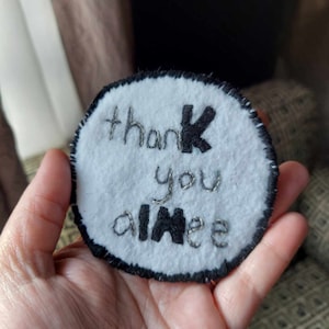 May include: A white felt circle with black embroidery that says "thank you aimee".