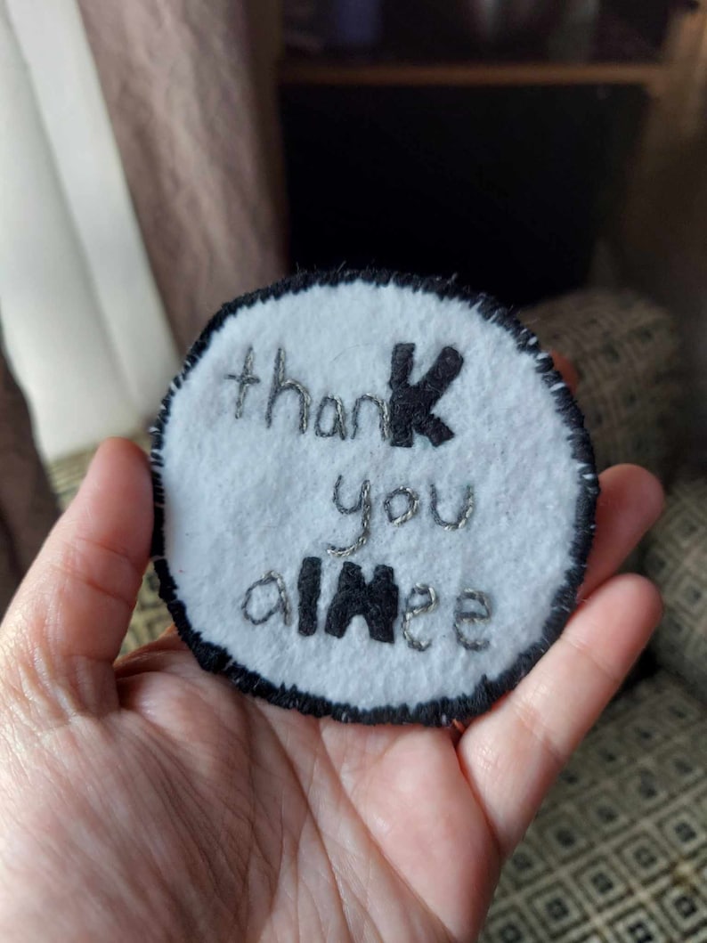 May include: A white felt circle with black embroidery that says "thank you aimee".