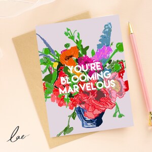 May include: A greeting card with a purple background and a bouquet of colorful flowers in a blue vase. The text on the card reads "You're Blooming Marvelous".