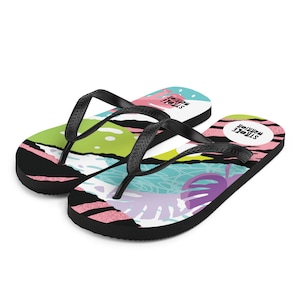 May include: A pair of black flip-flops with a colourful abstract print. The print features pink, green, blue, and white shapes and patterns. The flip-flops have the text "STROKE" and "PREVENTION" on the straps.