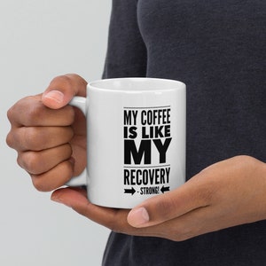 May include: White ceramic coffee mug with black text that reads "My coffee is like my recovery - strong!"