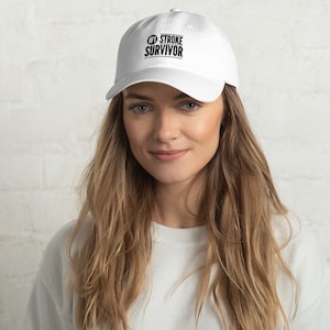 May include: White baseball cap with black embroidered text that reads "#1 STROKE SURVIVOR".