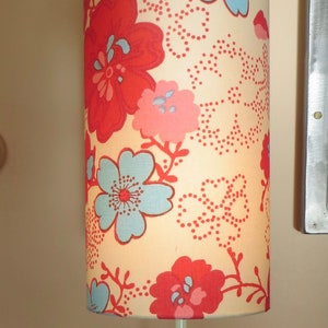 Peut inclure: Une lampe de table avec un abat-jour à motifs floraux dans des tons de rouge, rose et bleu. La lampe a une base bleue avec un design ondulé.