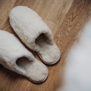 May include: A pair of white fluffy slippers on a wooden floor.