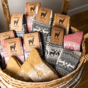 May include: A wicker basket filled with several pairs of alpaca wool socks. The socks feature various patterns, including snowflakes and reindeer, in colors like gray, red, and yellow. Each pair has a tag that reads "ALPAKA WOOL".