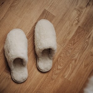May include: A pair of white fluffy slippers on a wooden floor.