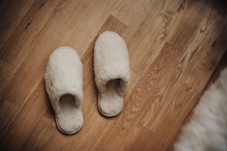 May include: A pair of white fluffy slippers on a wooden floor.
