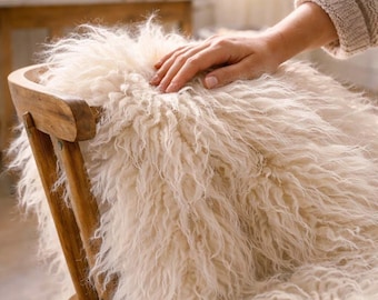 Può includere: Una pelle di pecora a pelo lungo color bianco sporco drappeggiata su una sedia in legno. Il vello presenta una consistenza folta e arruffata con riccioli naturali e un aspetto color crema morbido che copre la seduta e lo schienale della sedia.