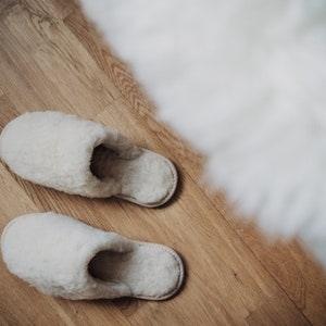 May include: Two pairs of white fluffy slippers on a wooden floor.