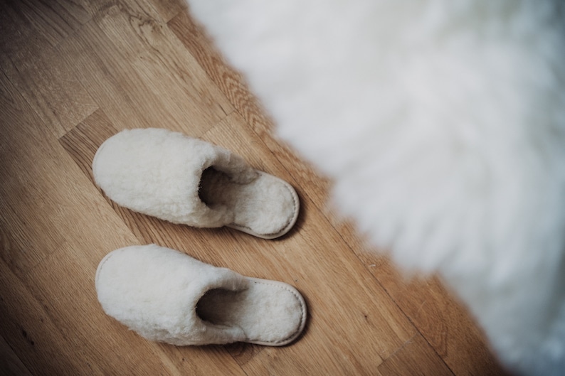 May include: Two pairs of white fluffy slippers on a wooden floor.