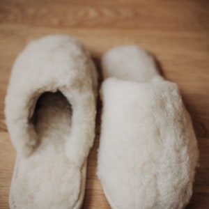 May include: A pair of white fluffy slippers with a closed toe and a soft, fuzzy texture.