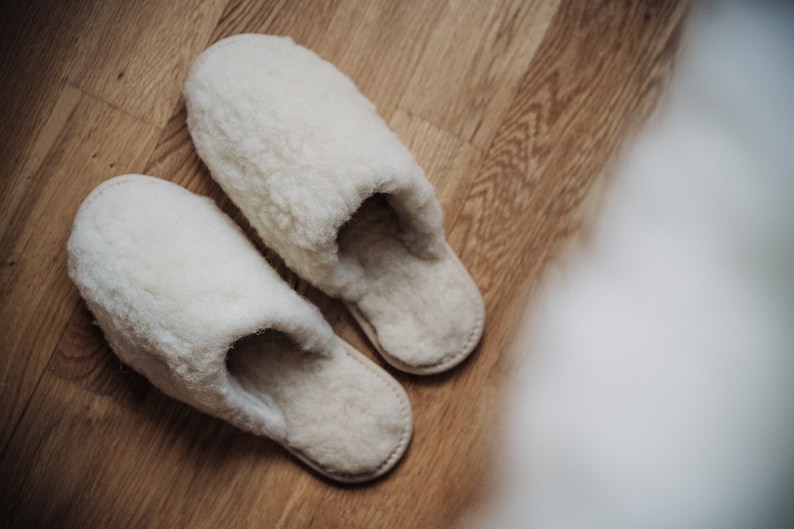 May include: A pair of white fluffy slippers on a wooden floor.